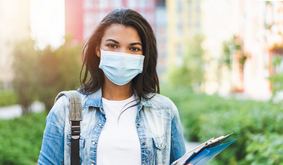 Female student walking to class wearing a surgical mask